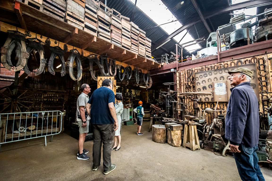 Visiteurs découvrant la collection d'outils anciens et fers à cheval dans la grange-musée