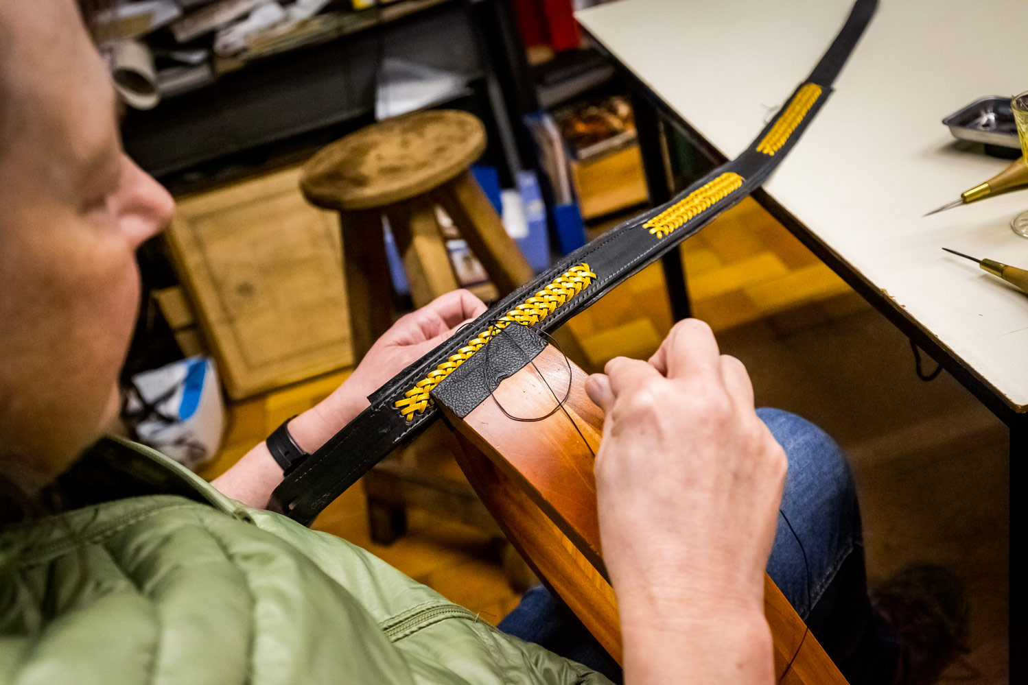 Artisan réalisant un laçage décoratif jaune sur fourreau cuir noir